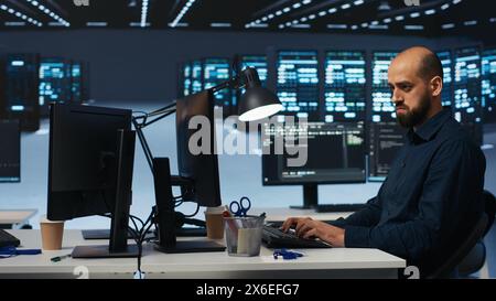 System admin focused on programming in server farm housing advanced equipment storing massive datasets. Developer typing code on PC to mend data center racks doing complex computational operations Stock Photo