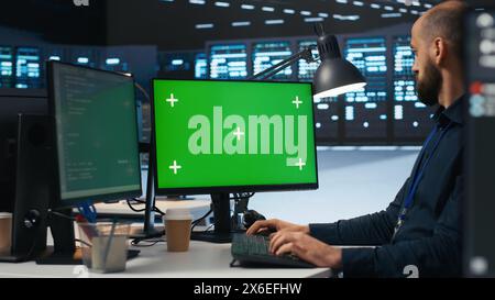 IT employee programming on green screen PC in data center housing supercomputers storing datasets. Admin writing code on mockup computer monitor to mend data center racks Stock Photo