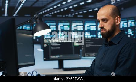 System admin focused on programming in server farm housing advanced equipment storing massive datasets. Developer typing code on PC to mend data center racks doing complex computational operations Stock Photo