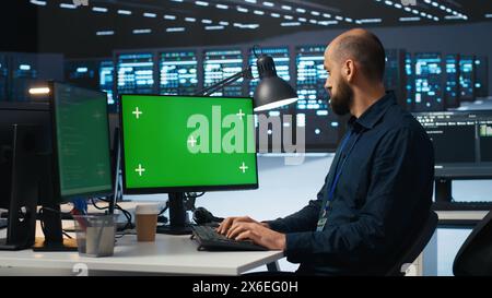 Man typing code on green screen computer in high tech data center with server rows providing computing resources. IT specialist using mockup PC to oversee rackmounts operating data Stock Photo