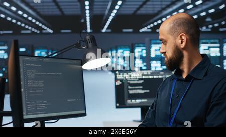 System administrator in server hub coding, ensuring data remains shielded from threats. IT developer safeguarding supercomputers against unauthorized access, securing system from hackers Stock Photo