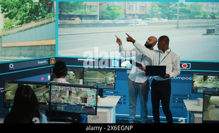 Diverse employees using CCTV surveillance system in monitoring traffic, tracking speed limits for public safety via satellite radar system. People operating on a big screen in control center. Camera B. Stock Photo