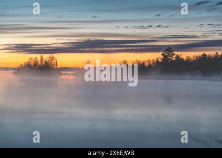 The sun rises in northern Minnesota near Duluth over a beautiful lake scene as steam rises from the calm water Stock Photo