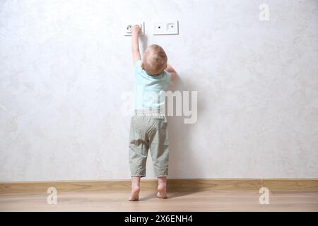 Little child playing with electrical socket indoors, back view. Dangerous situation Stock Photo