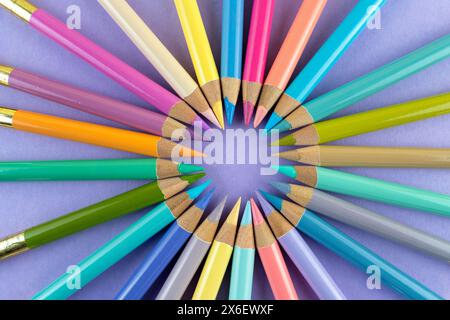 Colorful wooden crayons arranged in a circle on a purple paper background Stock Photo