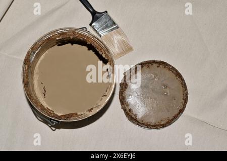 Rusted old metal paint tin with open lid paintbrush on drop cloth brown expired storage. Stock Photo