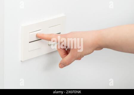 Close-up of woman hand turning on the light with a wall switch Stock Photo