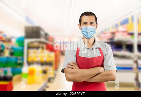 Business owner working with red apron at a supermarket wearing a facemask to avoid the coronavirus - pandemic lifestyle concepts and copy space. Stock Photo