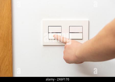 Close up of female finger is turn on or off on light switch with white wall at home copy space. Stock Photo