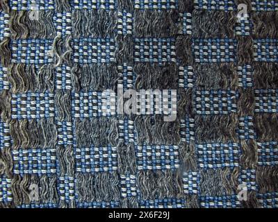 A handmade quilt, with white wool threads and various shades of blue, intertwined forming a tighter checkerboard and looser lines. Stock Photo