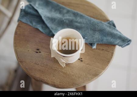 Takeaway black coffee in the paper cup on the wooden stool chair at the cafe. Stock Photo