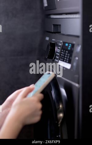 Woman controls washing machine with a phone. Stock Photo