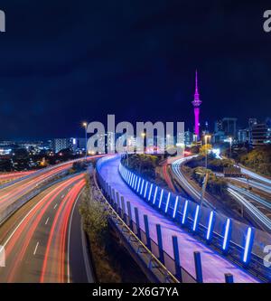 Sky Tower lit up in pink to celebrate Mother’s Day. Long exposure image with car light trails on motorways. Auckland. Stock Photo