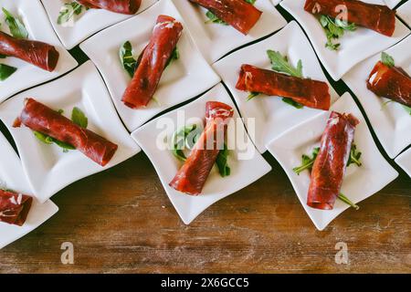 Elegant presentation of meat appetizers on a bed of greens, arranged in small white square plates, showcasing gourmet appetizers in a visually appeali Stock Photo