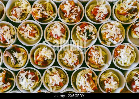 An arrangement of assorted gourmet appetizers, featuring individual cups with slices of bread topped with red sauce and grated cheese, perfect for par Stock Photo
