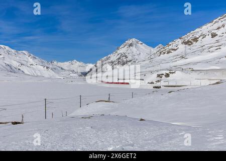 Bernina Pass with the little red train crossing the valley. Winter landscape, the mountains are covered in snow. Nobody inside Stock Photo