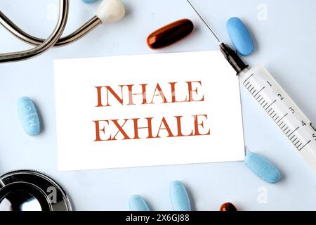 INHALE EXHALE written words on a business card on a blue background with a stethoscope, pills and a syringe in the composition Stock Photo