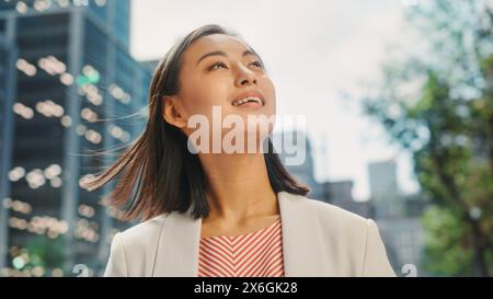 Portrait of Beautiful Japanese Female Wearing Smart Casual Clothes Posing on the Street. Successful Female in Big City Living the Urban Lifestyle. Background with Office Buildings and Billboards. Stock Photo