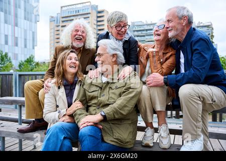 Group of elderly Caucasians friends people having fun laughing together sitting on bench in city. Stock Photo