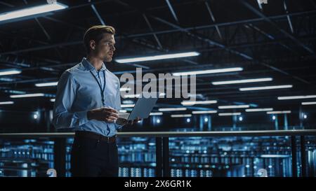 Data Center Specialist Engineer Using Laptop Computer. Server Farm Cloud Computing Facility with Male System Administrator Working. Data Protection Network for Cyber Security. Stock Photo