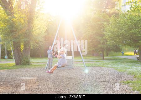 happy preschool girl swings high on summer day, blurred child figure in rays light, joyful Carefree childhood memories, vestibular apparatus training Stock Photo