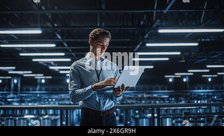 Portrait of IT Specialist Uses Laptop in Data Center. Server Farm Cloud Computing Facility with Male Maintenance Administrator Working. Cyber Security and Network Protection. Stock Photo