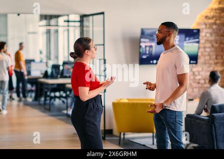 Young business colleagues, including an African American businessman, engage in a conversation about business issues in the hallway of a modern Stock Photo