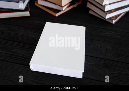 White book with space for text on a black table against the background of old books. Education concept Stock Photo