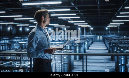 Portrait of IT Specialist Uses Laptop in Data Center. Server Farm Cloud Computing Facility with Male Maintenance Administrator Working. Cyber Security and Network Protection. Stock Photo