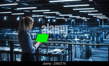 Female It Specialist Using Chroma Key Laptop in Data Center. Big Server Farm Cloud Computing Facility with Maintenance Engineer Working with Green Screen Computer. Stock Photo