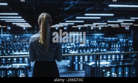 Data Center Female Programmer Using Laptop Computer, Maintenance IT Specialist. In Cloud Computing Server Farm Smiling System Administrator Working on Cyber Security for Iaas, saas, paas. Stock Photo