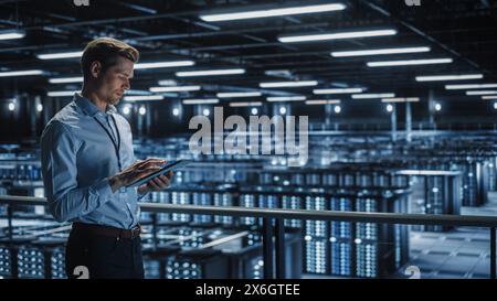 Portrait of IT Specialist Uses Tablet Computer in Data Center. Server Farm Cloud Computing Facility with Male Maintenance Administrator Working. Cyber Security and Network Protection. Stock Photo