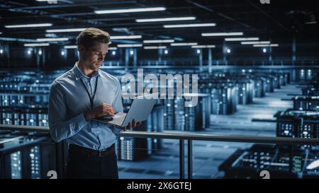 Portrait of IT Specialist Uses Laptop in Data Center. Server Farm Cloud Computing Facility with Male Maintenance Administrator Working. Cyber Security and Network Protection. Stock Photo