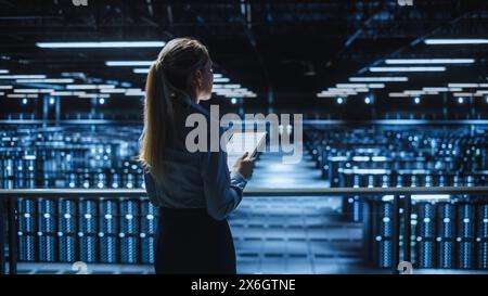 Data Center Female Programmer Using Tablet Computer, Maintenance IT Specialist. In Cloud Computing Server Farm Smiling System Administrator Working on Cyber Security for Iaas, saas, paas. Stock Photo