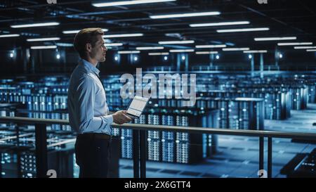 Data Center Specialist Engineer Using Laptop Computer. Server Farm Cloud Computing Facility with Male System Administrator Working. Data Protection Network for Cyber Security. Stock Photo