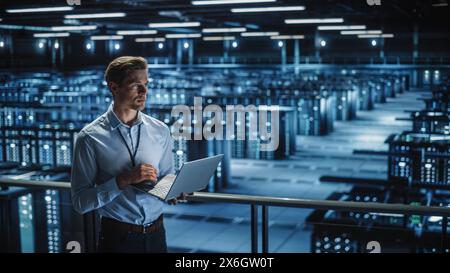 Data Center Specialist Engineer Using Laptop Computer. Server Farm Cloud Computing Facility with Male Maintenance Administrator Working. Data Protection Network for Cyber Security. Stock Photo