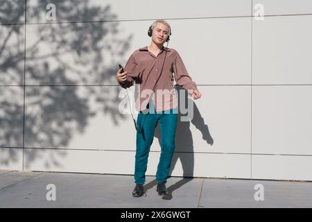 young man with short blonde hair, Latino of Argentine ethnicity, wearing vintage style clothing, is jumping outdoors enjoying sunset listening to musi Stock Photo