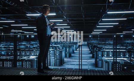 Portrait of IT Specialist Using Tablet Computer in Data Center. Big Server Farm Cloud Computing Facility with Male System Administrator Working. Cyber Security, Network Protection. Stock Photo