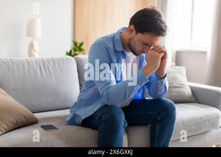 Man Sitting on Couch With Hands on Face Stock Photo