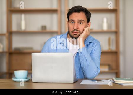 Bored Young Man Working on Laptop at Home During Daytime Stock Photo