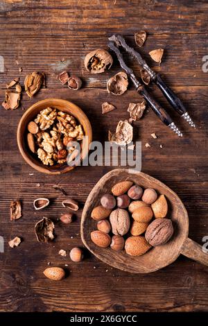 Seen from above, on an old wooden background, a nutcracker, a bowl with shelled walnuts and a wooden scoop contains mixed nuts Stock Photo