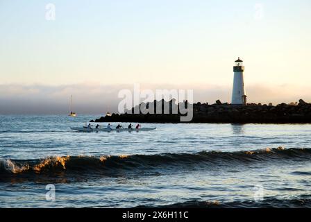 A crew rowing their canoe passes the Walton Lighthouse as they head into the channel from the sea in Santa Cruz, California Stock Photo