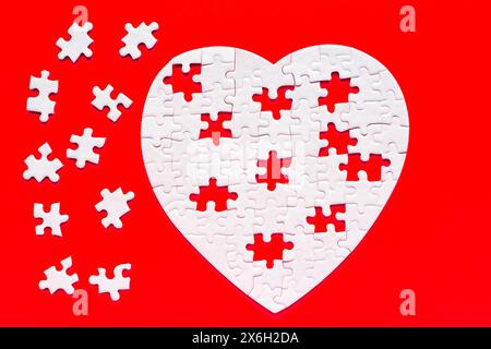 Incomplete heart-shaped puzzle set against a bold red backdrop. The missing puzzle pieces are scattered aside the heart. Stock Photo