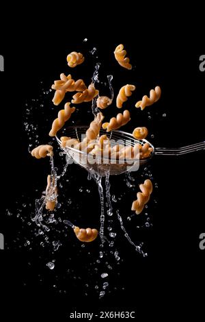 Wholemeal fusilli, Italian pasta floating and dripping on a black background. Stock Photo