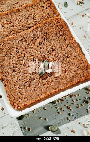 some slices of rye bread with flax seeds in a white rectangular ceramic plate placed on a gray textured surface Stock Photo