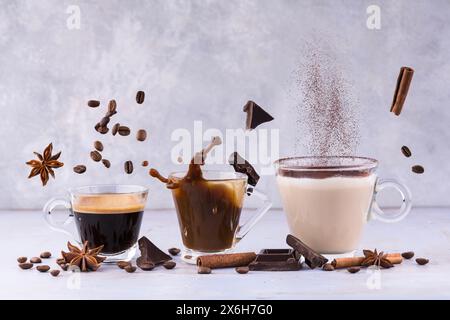 lively composition with espresso, latte and cappuccino in transparent glass cups among floating aromatic spices, chocolate pieces and coffee beans Stock Photo