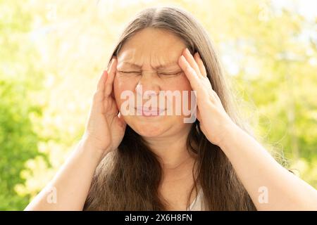 diseased mature woman experiences severe headache, holding head, Hot flashes during menopause, Decreased memory and concentration, feeling nervous, ti Stock Photo