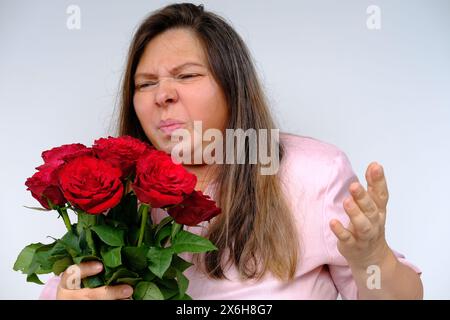 bouquet of flowers, red roses, middle-aged woman 50 years old with bulging eyes from bewilderment and surprise, dissatisfaction with gift, flower poll Stock Photo