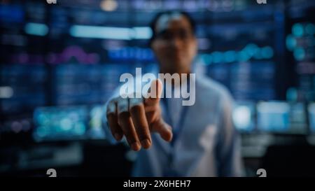 Shot with Focus on Finger of a Professional IT Technical Support Specialist or Software Developer Pushing an Augmented Reality Display in Control Room Full of Computers. Shot iwth Blurred Background. Stock Photo