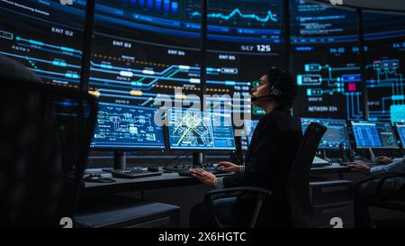 Professional IT Technical Support Specialists and Software Programmer Working on Computers in Monitoring Control Room with Digital Screens with Server Data, Blockchain Network and Surveillance Maps. Stock Photo